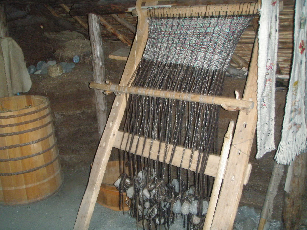 A loom with fabric being woven and the warp threads are weighted down with stones.